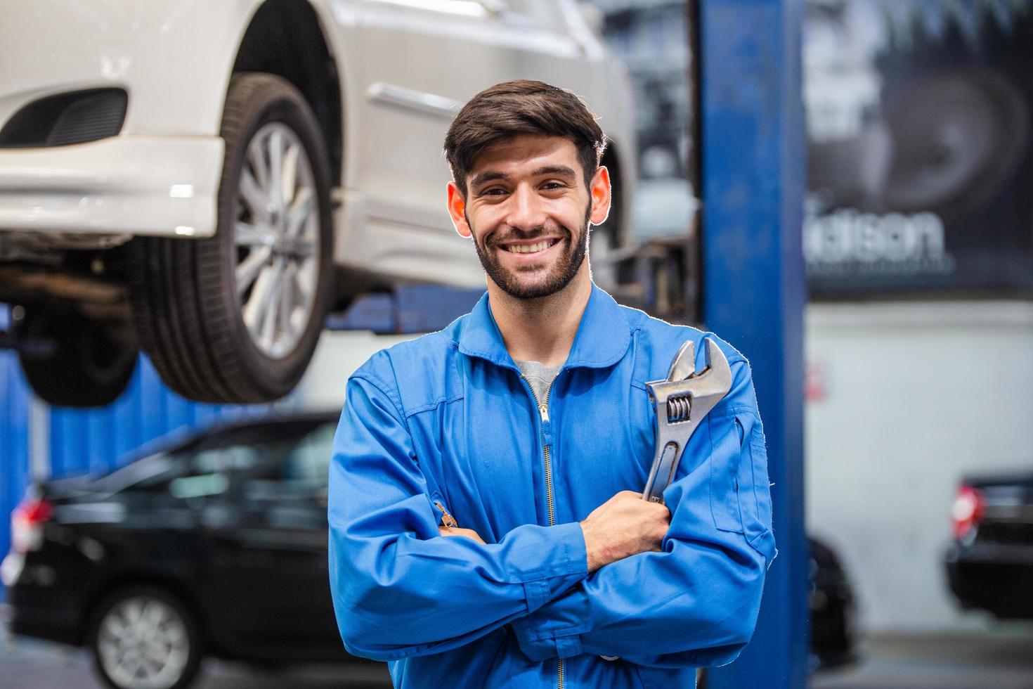 portrait of smiling male mechanic technician holding wrench in arms crossed at auto garage repair and maintenance career after service checking car damage broken part free photo
